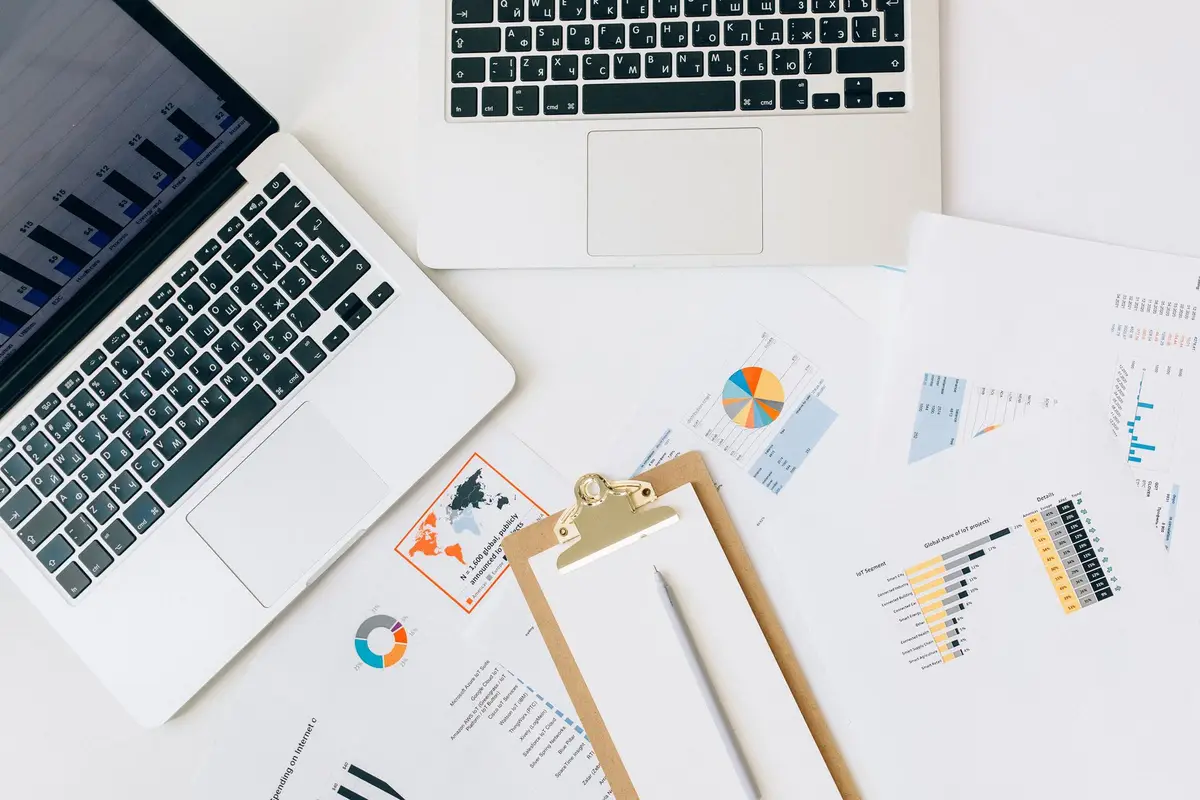 Person writing a business plan at a desk with a laptop and printed financial documents