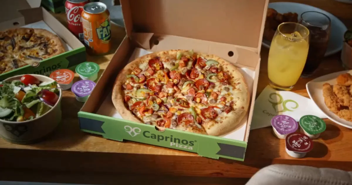 Caprinos Pizza branded takeaway box with a freshly cooked pizza inside, served alongside a side salad, soft drinks and dipping sauces - a typical Caprinos meal-deal at home