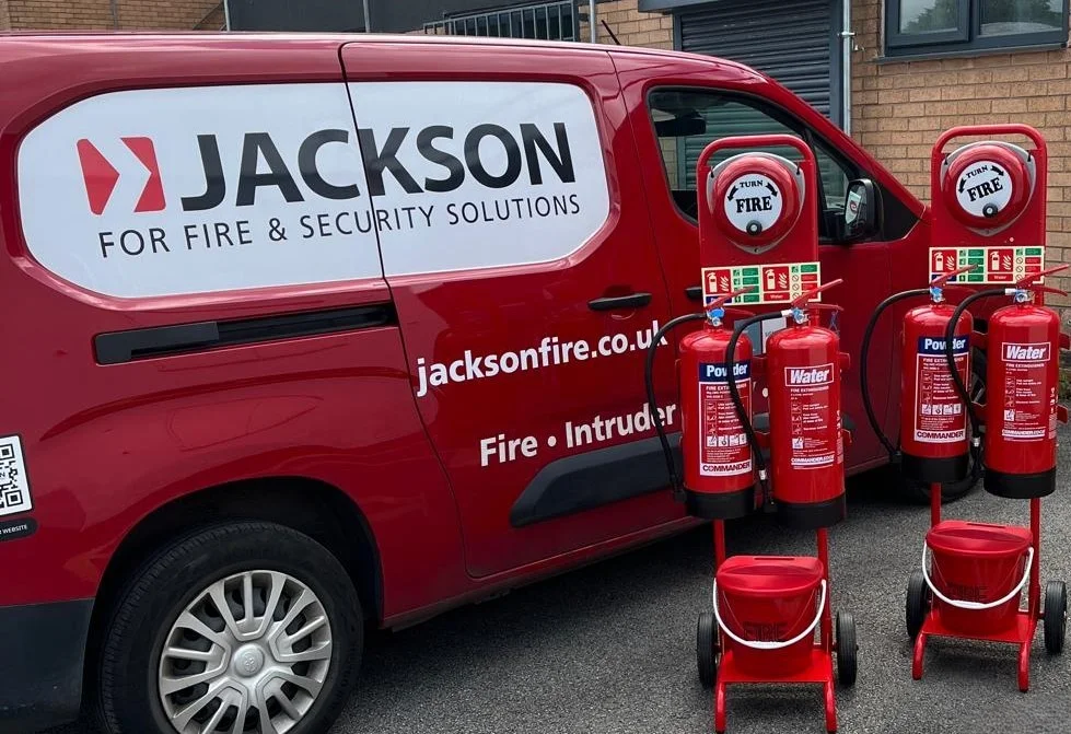 Jackson Fire & Security branded van parked alongside red Powder and Water fire extinguishers on commissioning trolleys, ready for site delivery and servicing