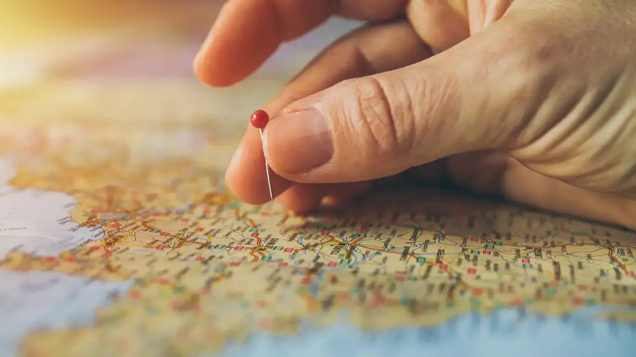 Hand placing a red pin on a UK map to represent franchise location choice
