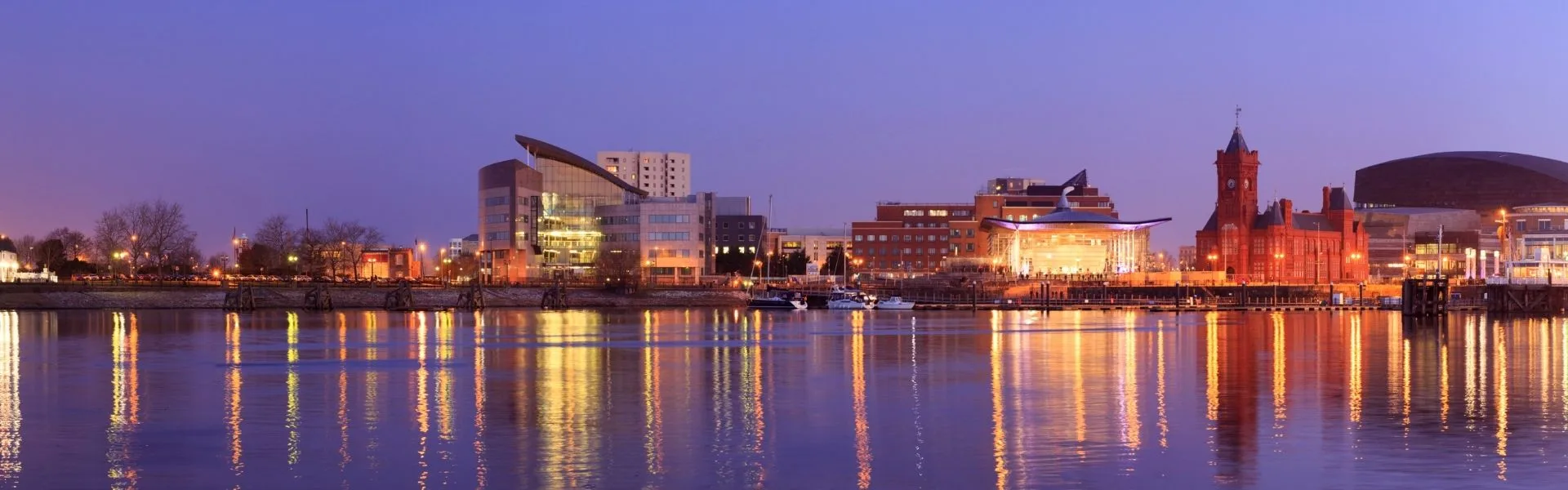 Cardiff Bay waterfront at dusk with the Pierhead Building, Wales Millennium Centre and city lights reflecting on the water, representing franchise opportunities in Wales.