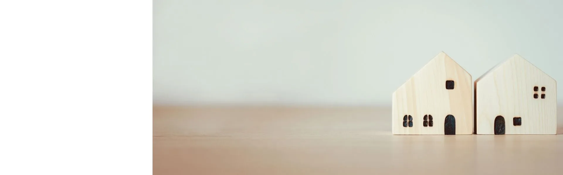 Two small wooden house models sitting side by side on a wooden surface against a soft neutral background, representing home-based franchise opportunities in the UK.